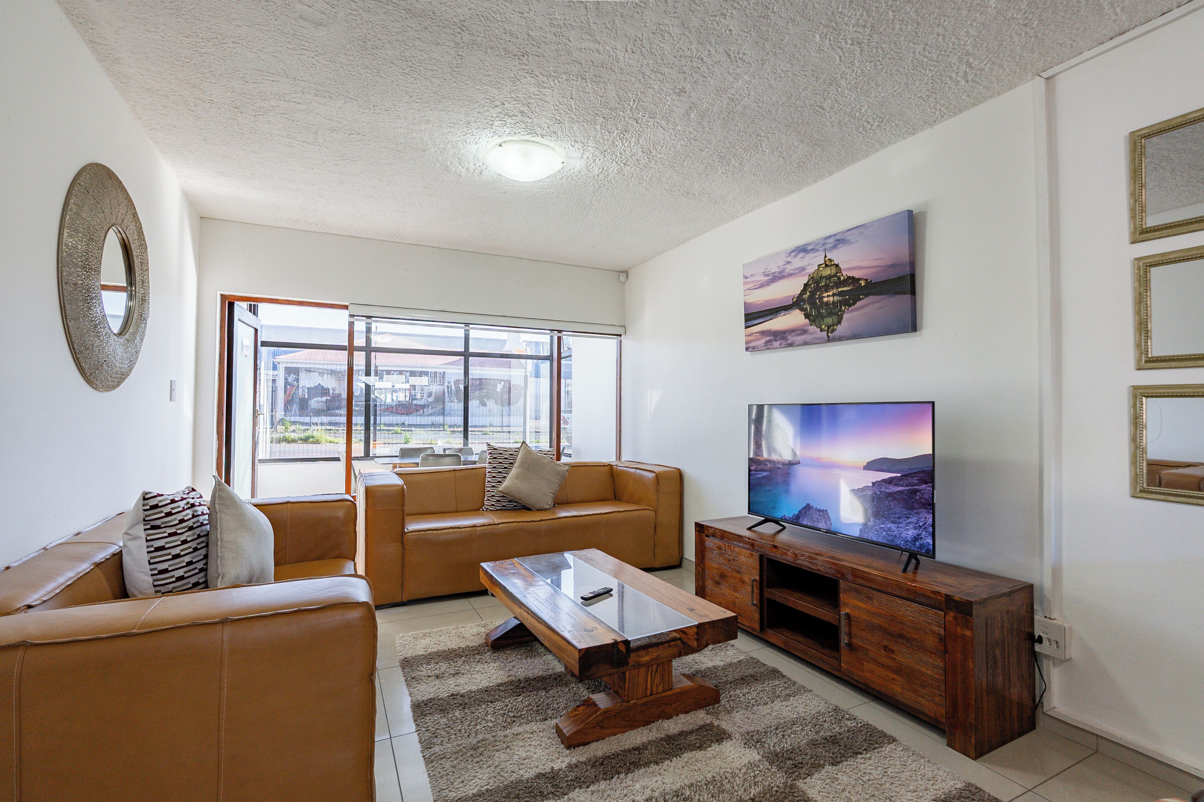 A living room with a sofa, a coffee table, a TV on a wooden stand, and a large window.