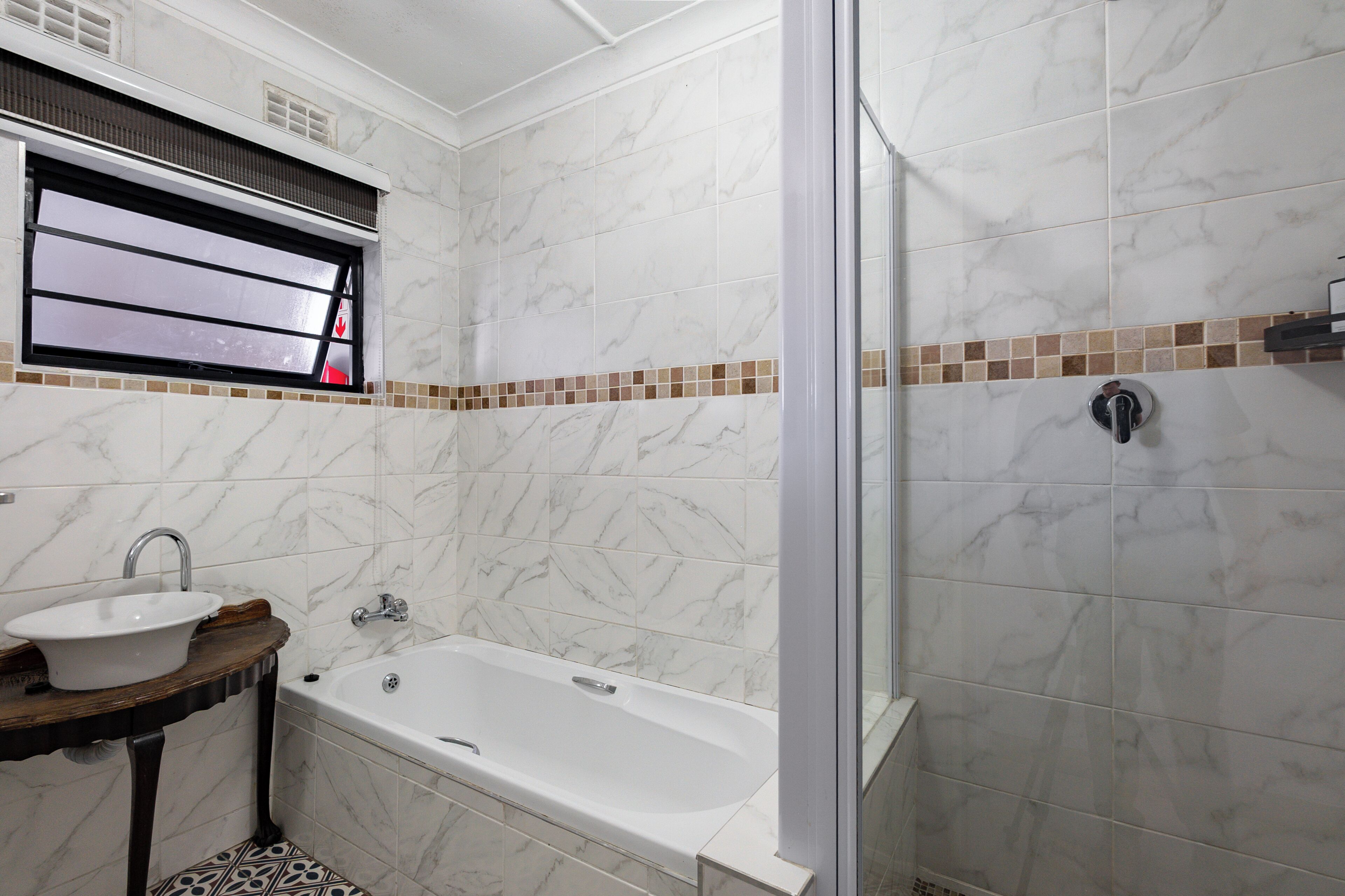 A bathroom with a bathtub, a sink, a shower, and a window with blinds.