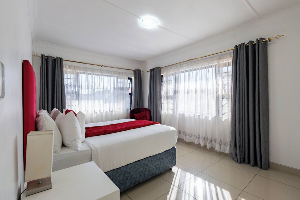 Una habitación de hotel con cama, mesita de noche, una silla y cortinas.
