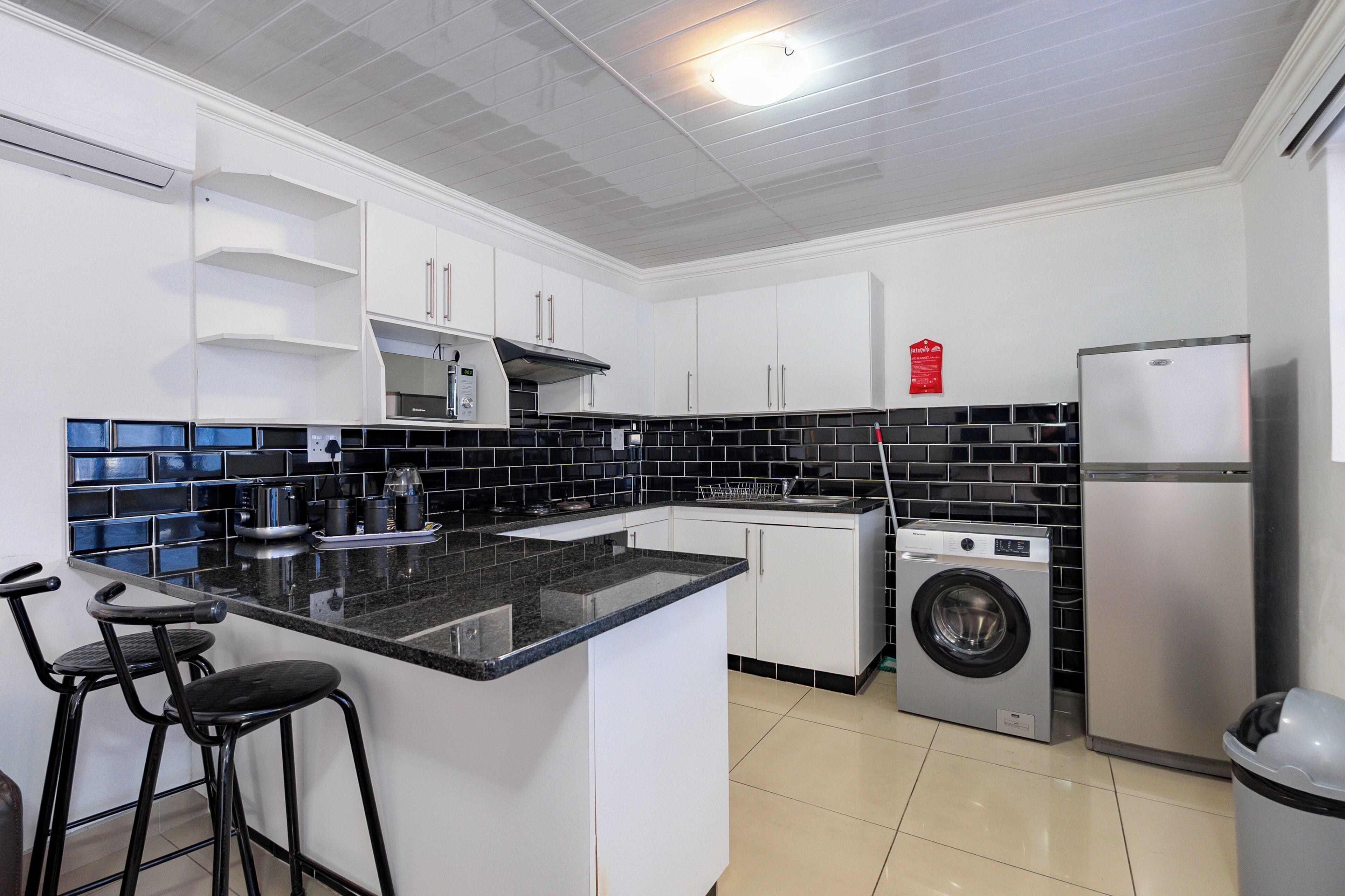 A kitchen with a washing machine, a refrigerator, and a bar stool.