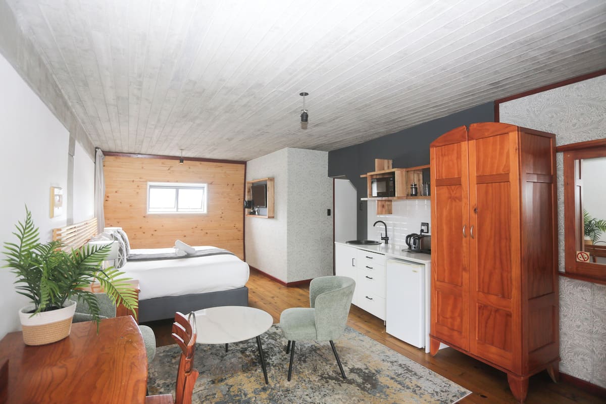 Un dormitorio moderno con techo de madera, una cama, una mesita de noche y una planta en maceta.