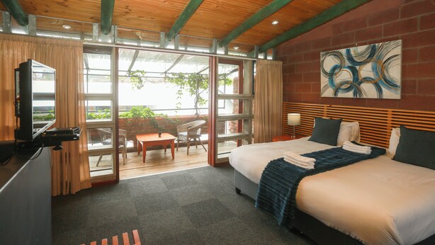 A hotel room with a bed, a desk, a chair, a large window, and a painting on the wall. - Safi Self-Catering Suites (East London)