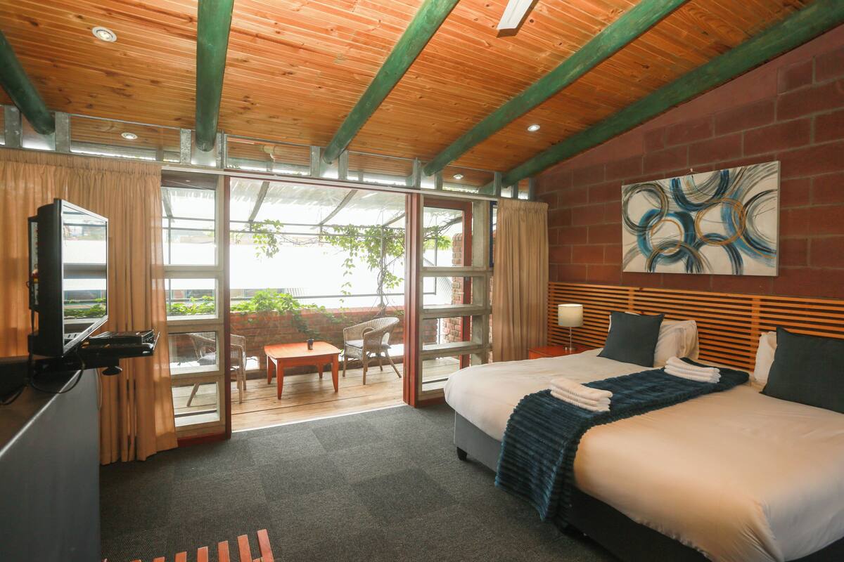 Habitación de hotel con cama, escritorio, silla, ventana grande y un cuadro en la pared.