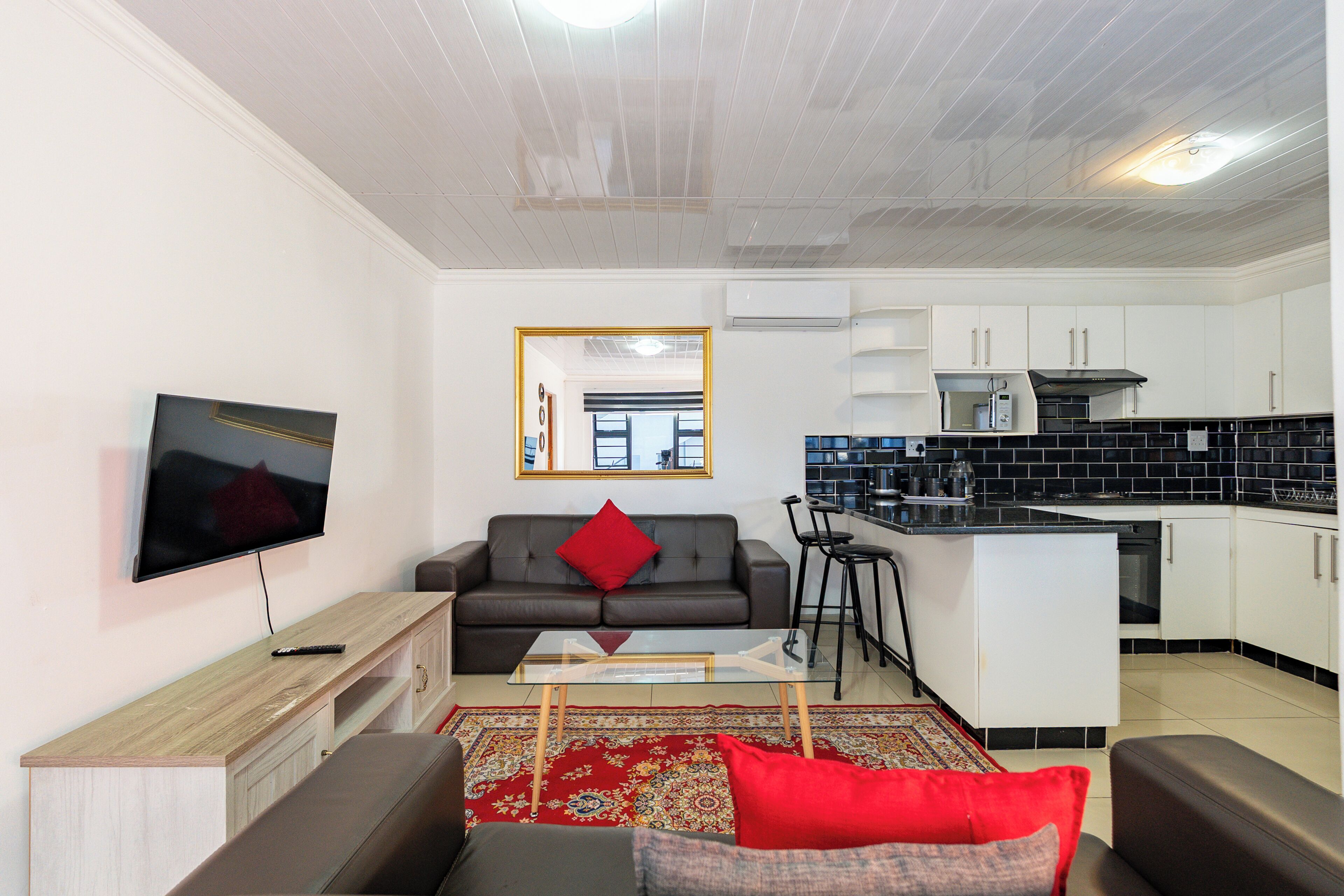Una sala de estar moderna con un televisor de pantalla plana, un sofá, una mesa de centro y una cocina con armarios blancos y baldosas negras.
