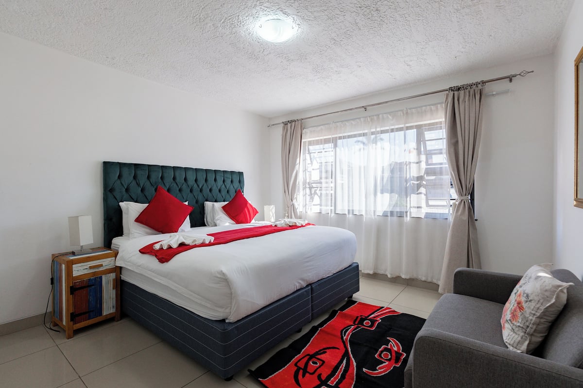 Un dormitorio con cama, mesita de noche, sofá y ventana con cortinas.