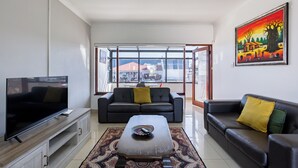 A living room with a TV, two sofas, a coffee table, and a large window. - Safi Self-Catering Suites (East London)