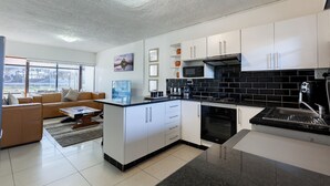 A modern kitchen with white cabinets, a black tiled backsplash, and a built-in microwave. - Safi Self-Catering Suites (East London)