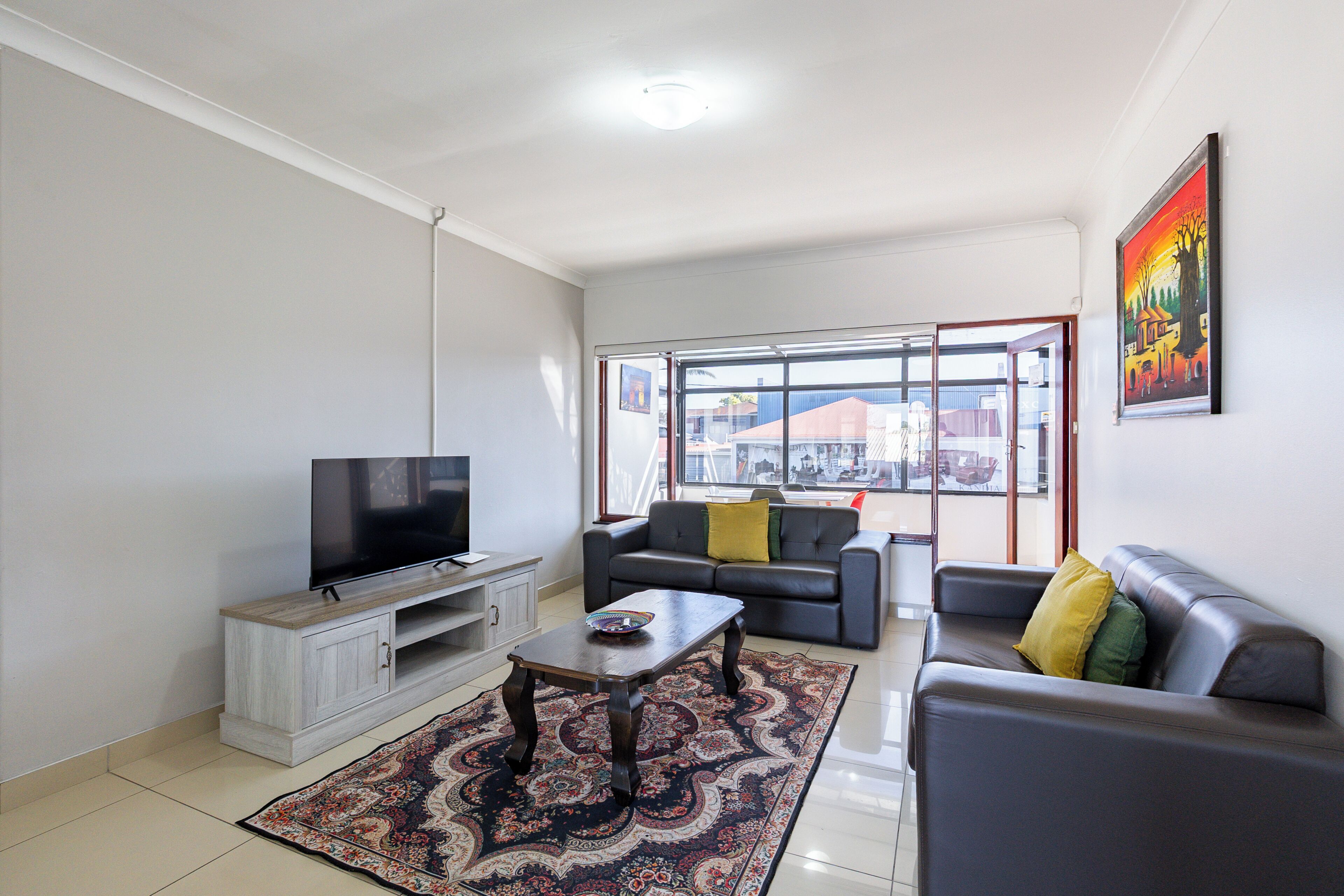 A living room with a flat-screen TV, a sofa, a coffee table, and a patterned rug.