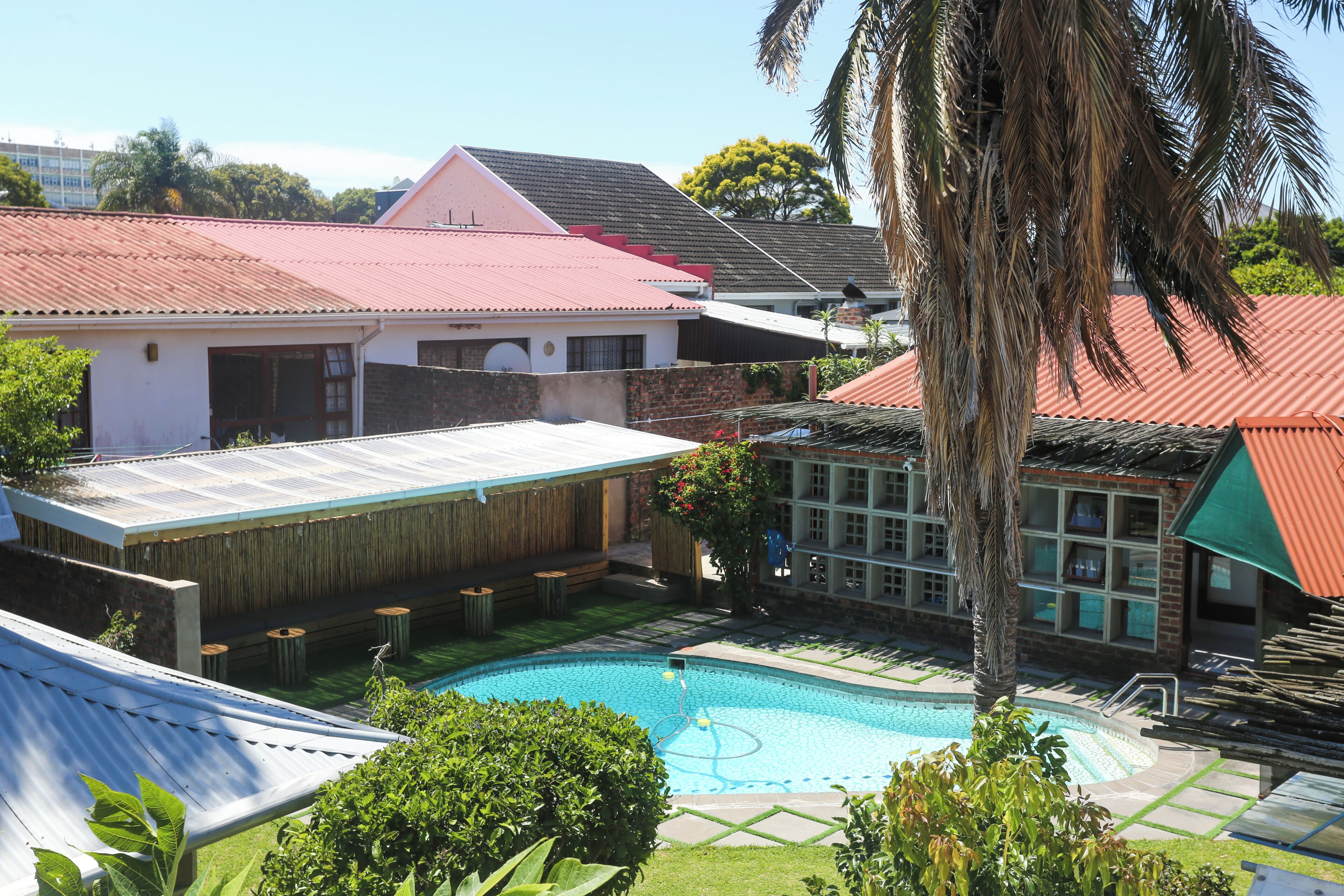 A residential area with a swimming pool, a house with a red roof, and a palm tree.
