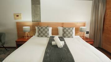 A hotel room with a large bed, wooden headboard, two bedside tables with lamps, and a grey patterned pillow.