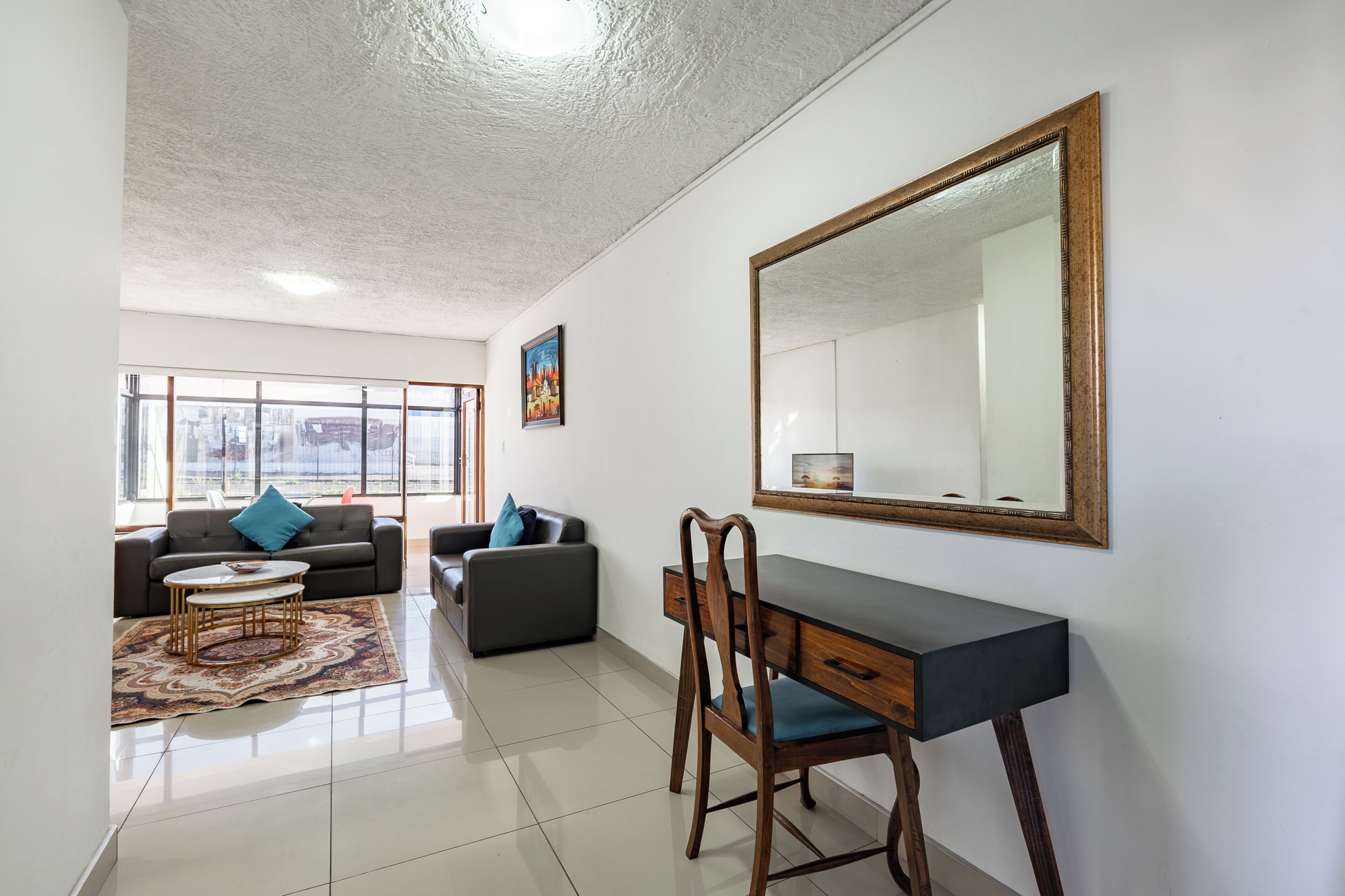A modern living room with a desk, two sofas, a coffee table, and a large mirror on the wall.