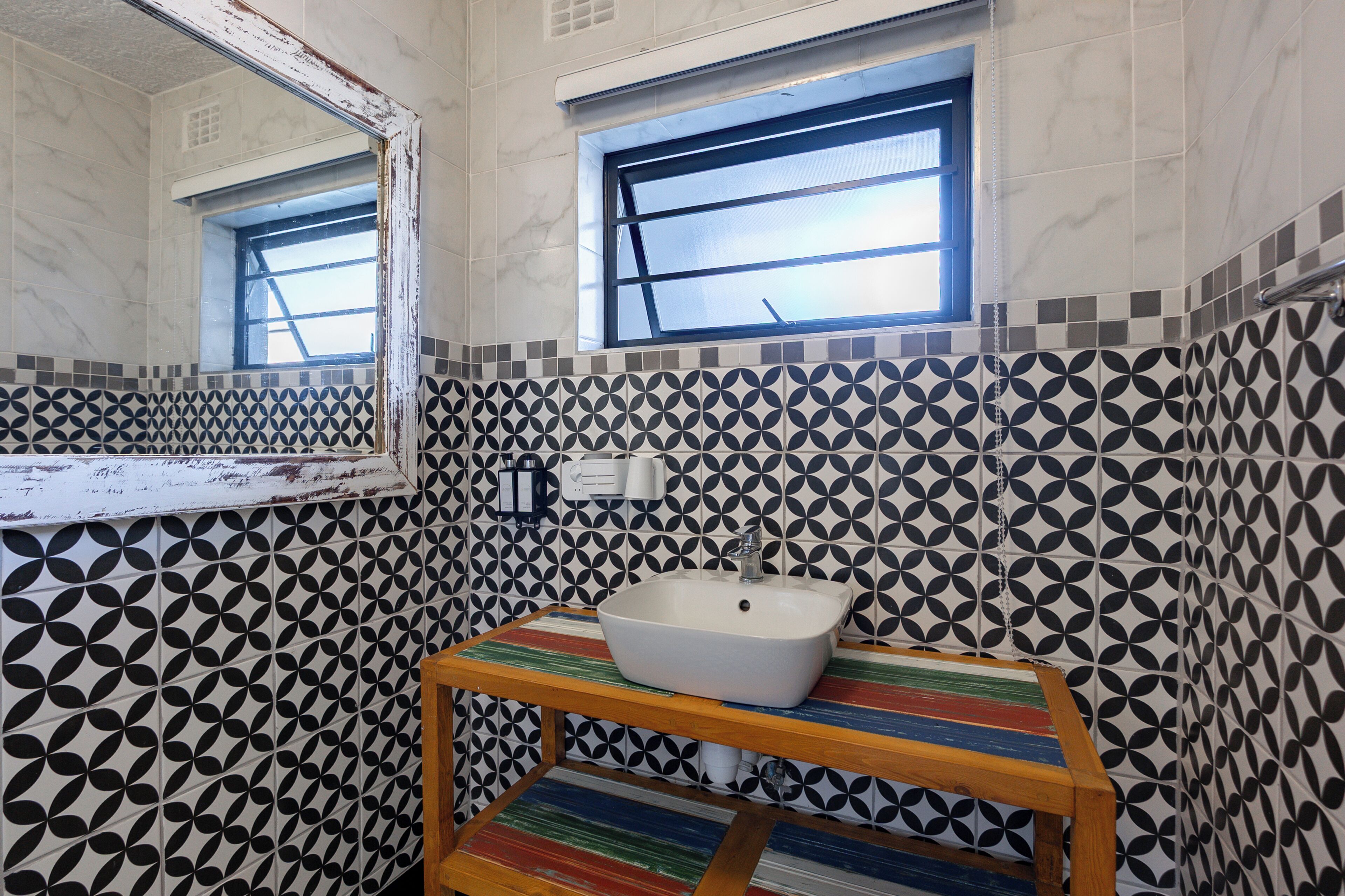 Une salle de bain avec un mur carrelé, une fenêtre, un lavabo et un miroir.