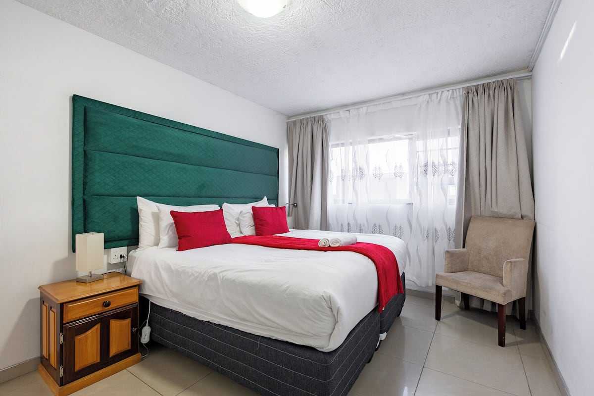 Una habitación de hotel ordenada con cama, mesita de noche, silla y cortinas.