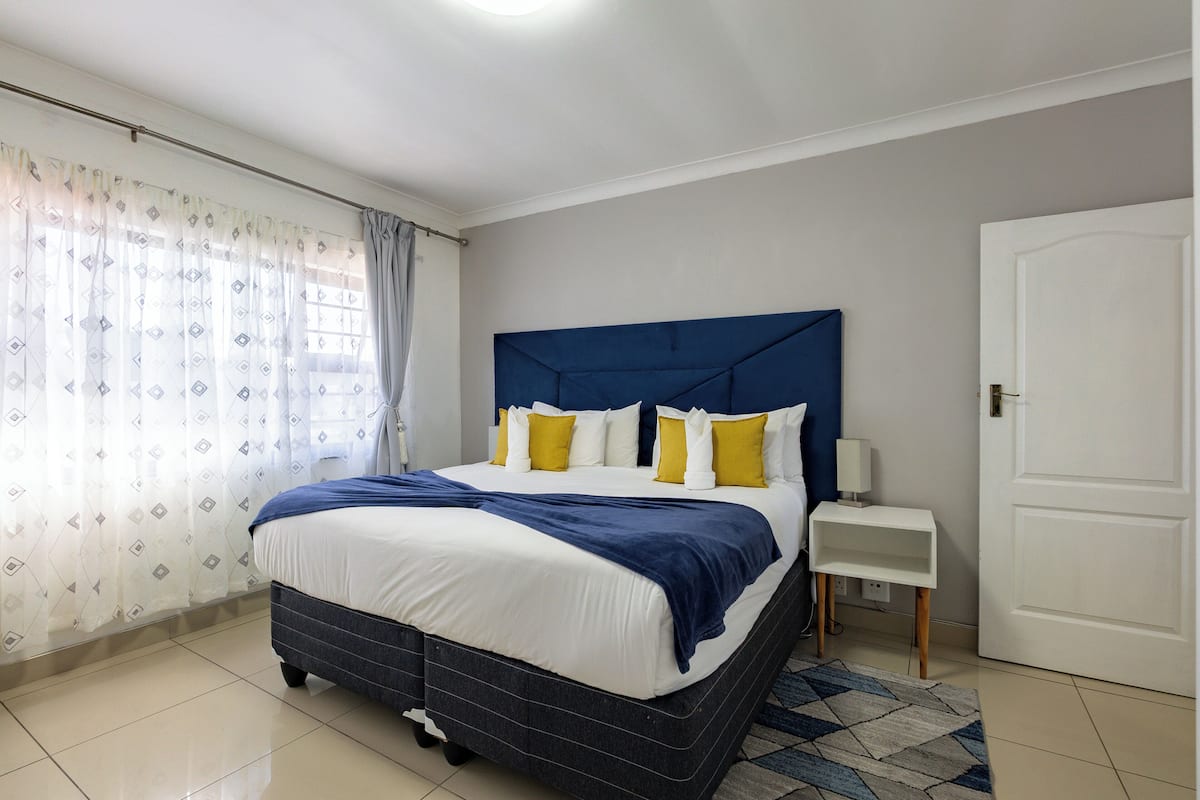 Un dormitorio con cama, cortinas, una mesita de noche y una puerta.