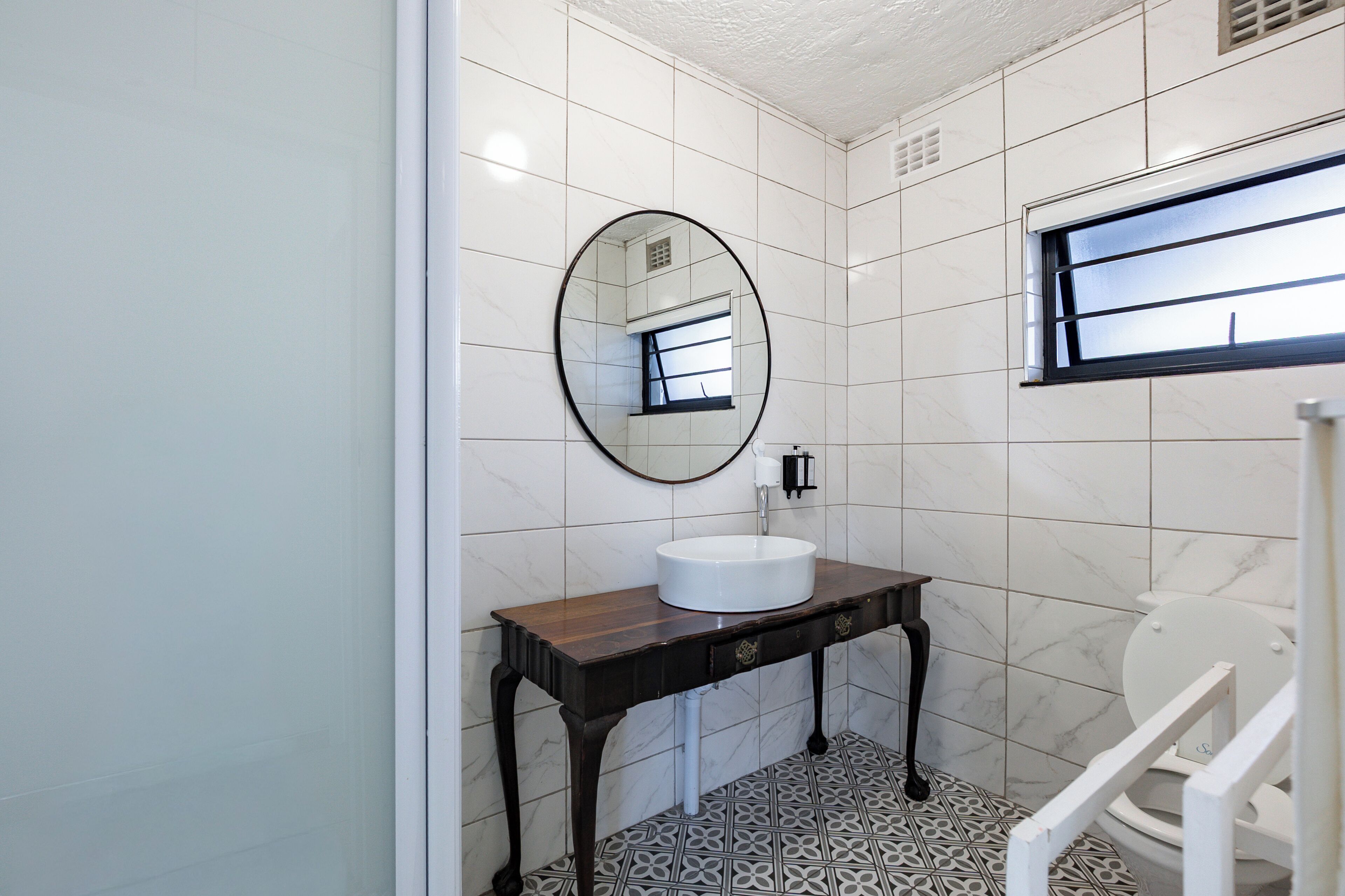 Un baño con lavamanos blanco, un espejo y una ventana.