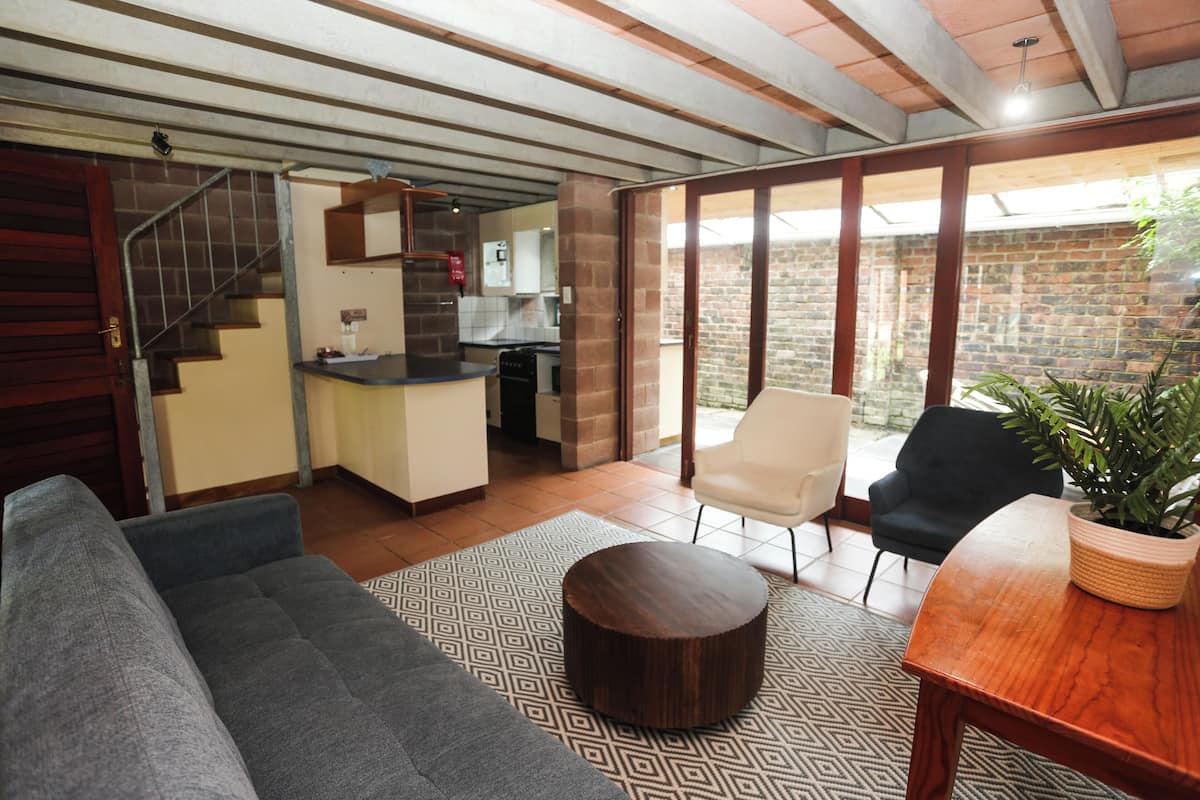 Una sala de estar con un sofá, una mesa de centro redonda, una mesa de comedor con sillas, una escalera y un área de cocina.