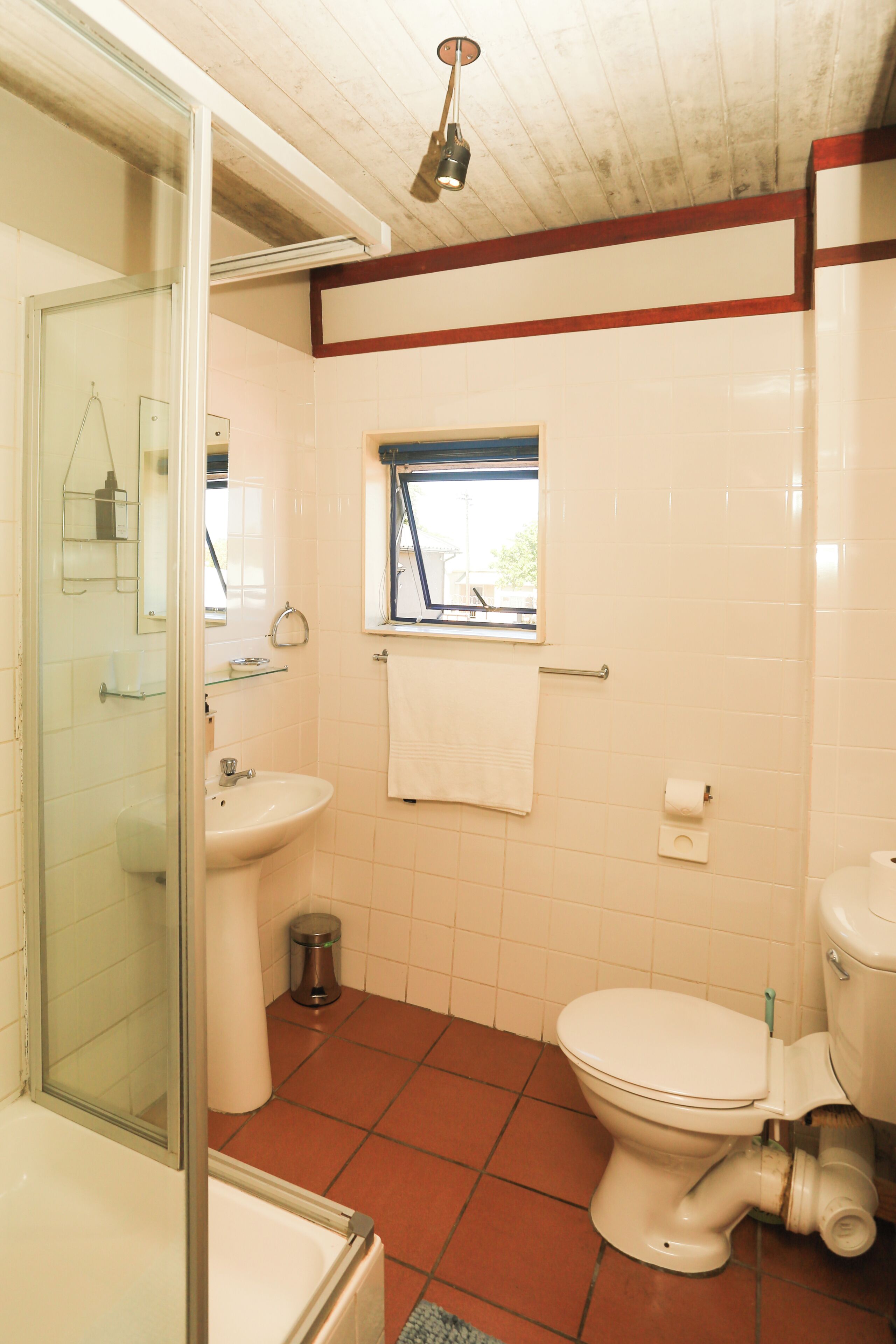 Une salle de bain avec une douche à parois de verre, un lavabo blanc, des toilettes et une fenêtre.