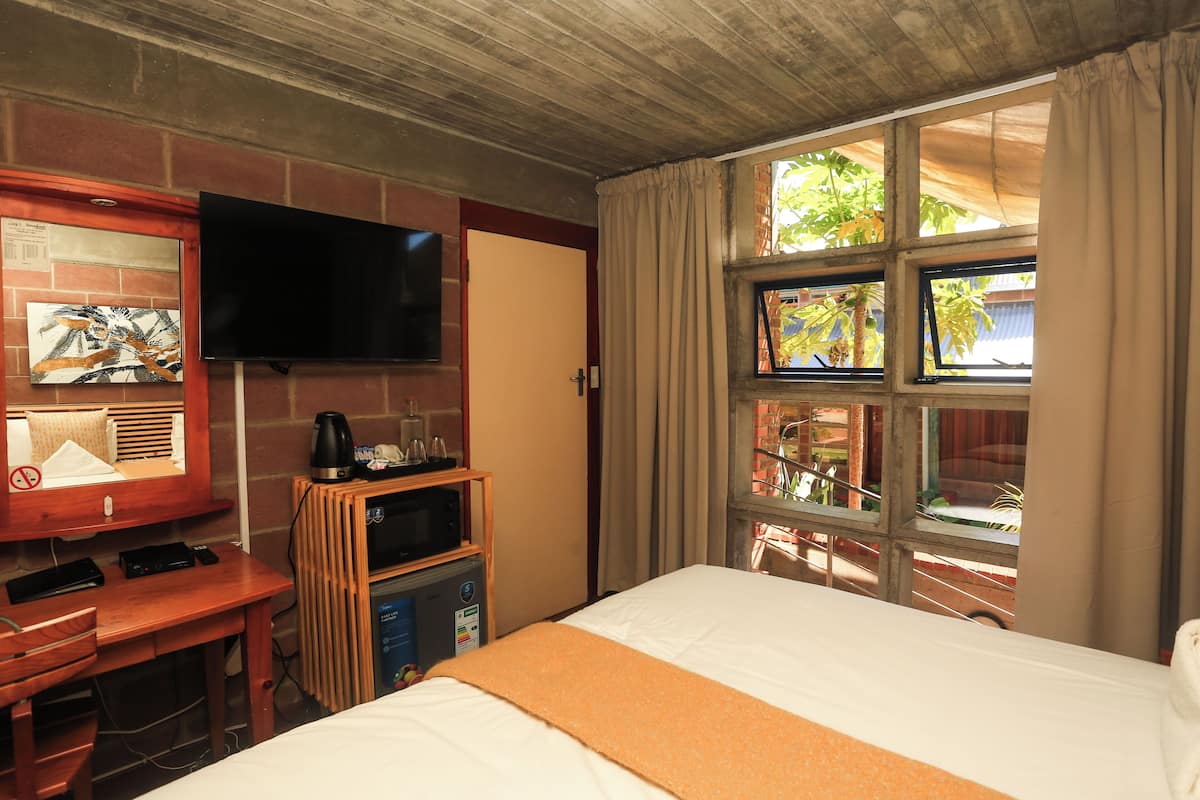 Una habitación de hotel con una cama, un televisor en la pared, un escritorio con cafetera y una ventana con cortinas.