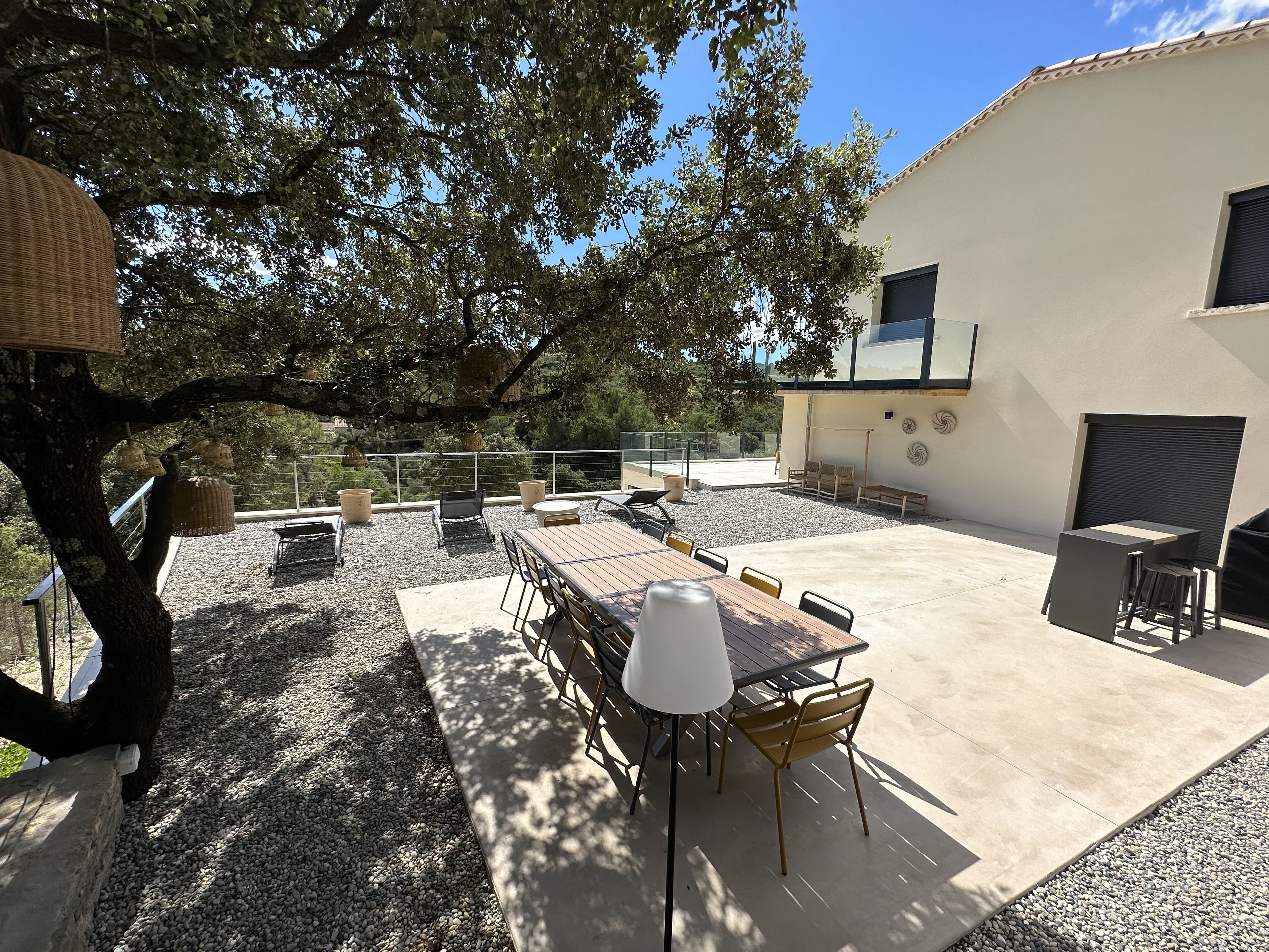 A patio with a wooden table and chairs, surrounded by a gravel area and a tree.