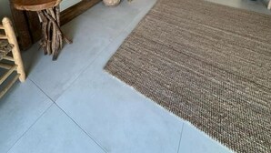 Een ruime woonkamer met een grote spiegel, een houten tafel, een geweven vloerkleed, en een moderne keuken op de achtergrond.