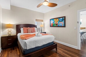 Un dormitorio con cama, mesitas de noche, ventilador de techo, un cuadro y vistas a otra habitación.