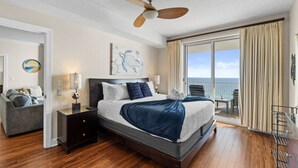 A bedroom with a bed, a nightstand, a lamp, a ceiling fan, a view of the ocean, and a balcony with a chair. - Ocean Ritz 2 Primary Suites | Expansive Balcony | Sleeps 12 (Panama City Beach)