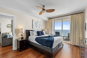 Ein Schlafzimmer mit Bett, Nachttisch, Lampe, Deckenventilator, Meerblick und einem Balkon mit Stuhl.