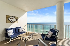 A balcony with a sofa, chairs, and a table, overlooking a clear blue sea.