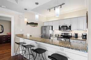A modern kitchen with granite countertops, stainless steel appliances, and bar stools.
