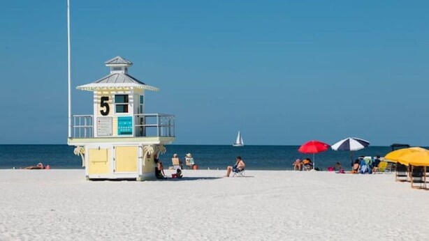 Ein Rettungsturm mit der Nummer 5, Strandkörbe und Menschen, die am Strand entspannen.