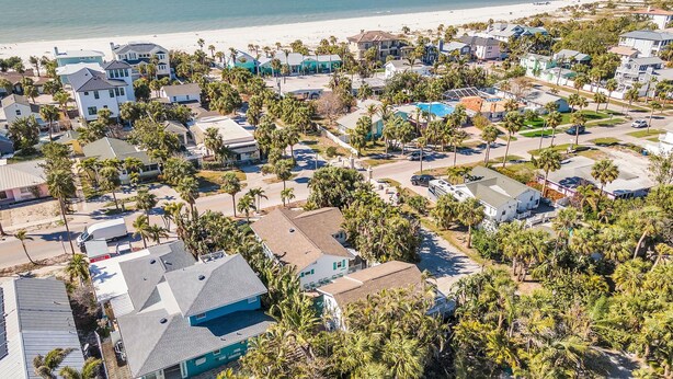 Vue aérienne d’un quartier résidentiel situé sur la côte, avec des maisons, des palmiers et une plage en arrière-plan.