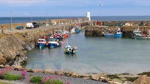 A harbor with boats docked, a lighthouse, and a stone wall. - Shoreline House (Fraserburgh)