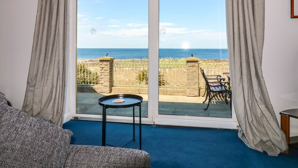 A room with a large sliding glass door leading to a balcony with a view of the sea. - Shoreline House (Fraserburgh)