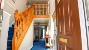 A hallway with a wooden staircase, a blue carpet, and a brown door. - Shoreline House (Fraserburgh)