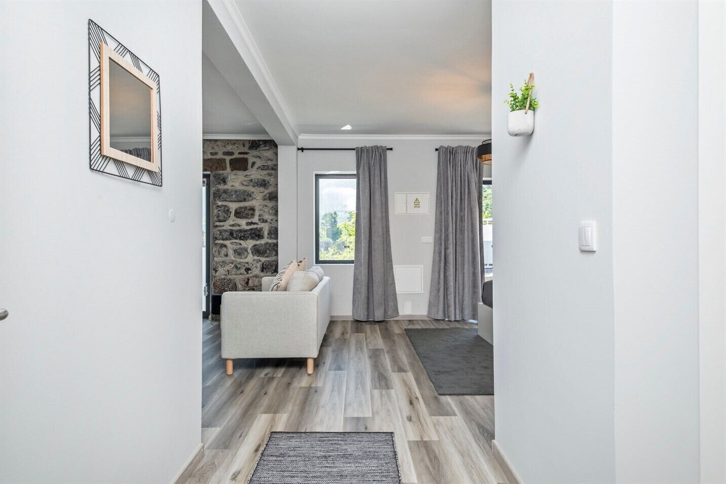 Un pasillo con pared de piedra, sofá blanco, cortinas grises y suelo de madera.