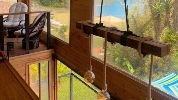A wooden cabin interior with a dining area, large windows, and a hanging light fixture.