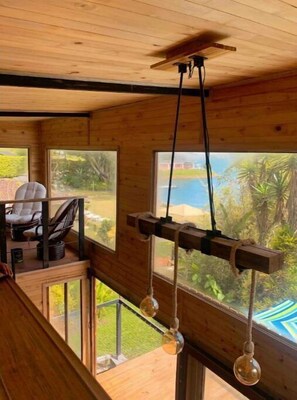 A wooden cabin interior with a dining area, large windows, and a hanging light fixture. - Casa Tulum Borde del Lago Calima con Jacuzzi (Calima)