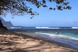 Une plage avec un ciel dégagé, des vagues et des gens dans l’eau.