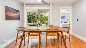 Een eethoek met een houten tafel en stoelen, een plafondventilator en uitzicht op groen via een glazen deur.