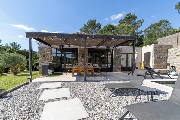 A modern outdoor patio with a pergola, seating area, and a pool.