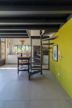 A modern kitchen with a yellow accent wall, a dining area with a table and chairs, and a staircase leading to another level.