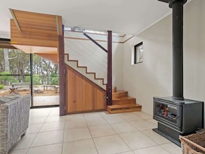 A modern interior with a wooden staircase, a fireplace, and a view to an outdoor area.