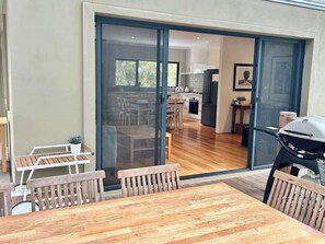 A modern kitchen with a dining area, sliding glass doors leading to a patio, and a barbecue grill.