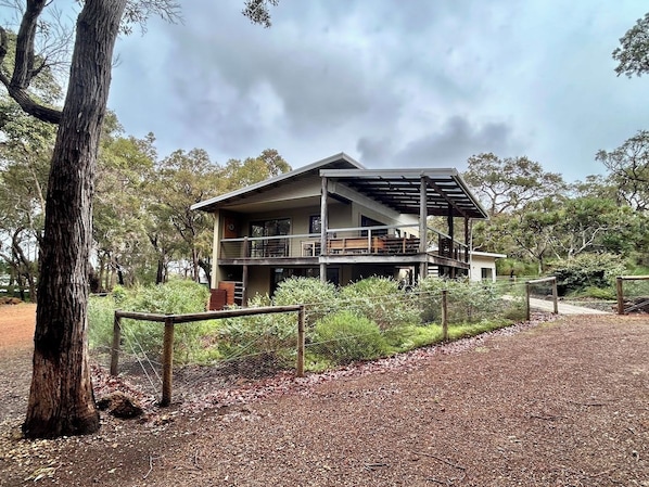 A two-story building with a balcony, surrounded by trees and a fence.