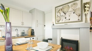 Una cocina moderna con armarios blancos, encimera de madera, chimenea con revestimiento de piedra y una obra enmarcada sobre la repisa.
