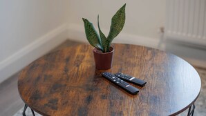 Una mesa redonda de madera con dos controles remotos y una planta en maceta.
