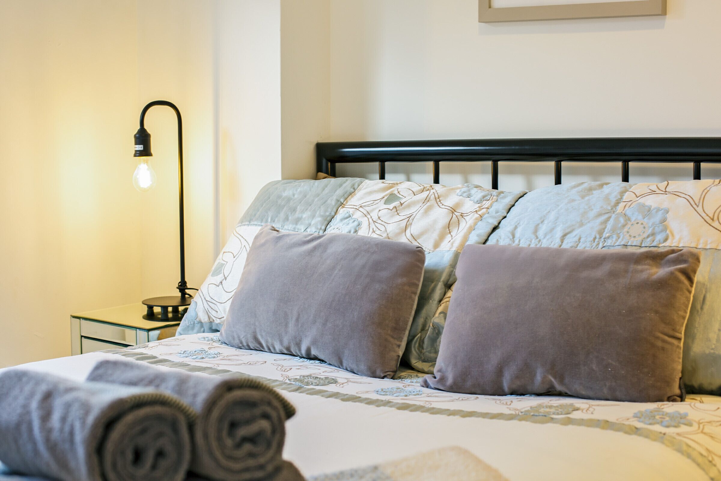 Un lit bien fait, avec une couvre-lit à motifs, deux oreillers et des serviettes enroulées.