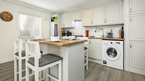 Una cocina moderna con armarios blancos, encimera de madera, lavadora integrada y un reloj en la pared.