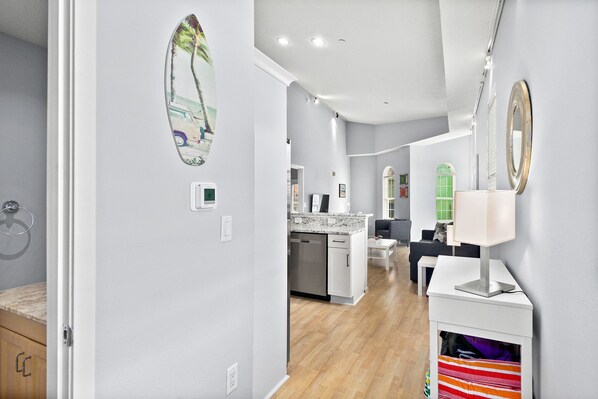 A modern kitchen with a marble countertop, a dishwasher, and a sink. There is a dining area with a table and chairs, and a kitchen island with a lamp.