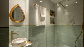 Un baño moderno con tocador de mármol, accesorios dorados y ducha con cabezal de lluvia.